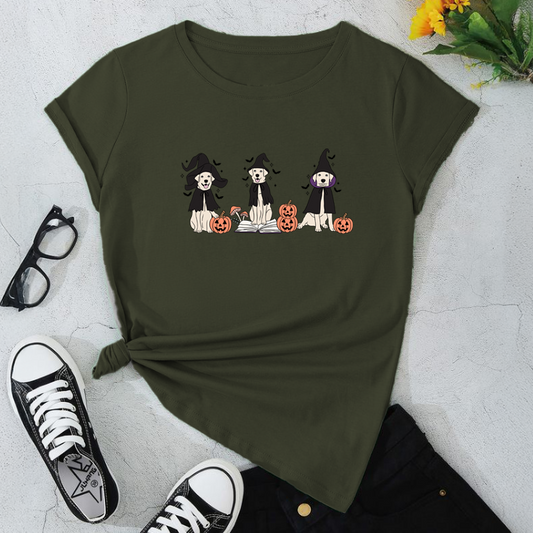Green t-shirt with Halloween-themed design of dogs in costumes on a light gray surface with sneakers and glasses.